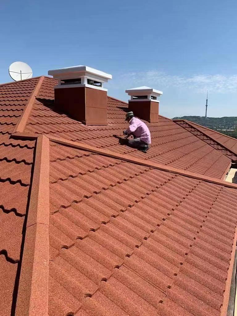 Un trabajador trabajador está absorto en la instalación de tejas metálicas revestidas de piedra en el techo.