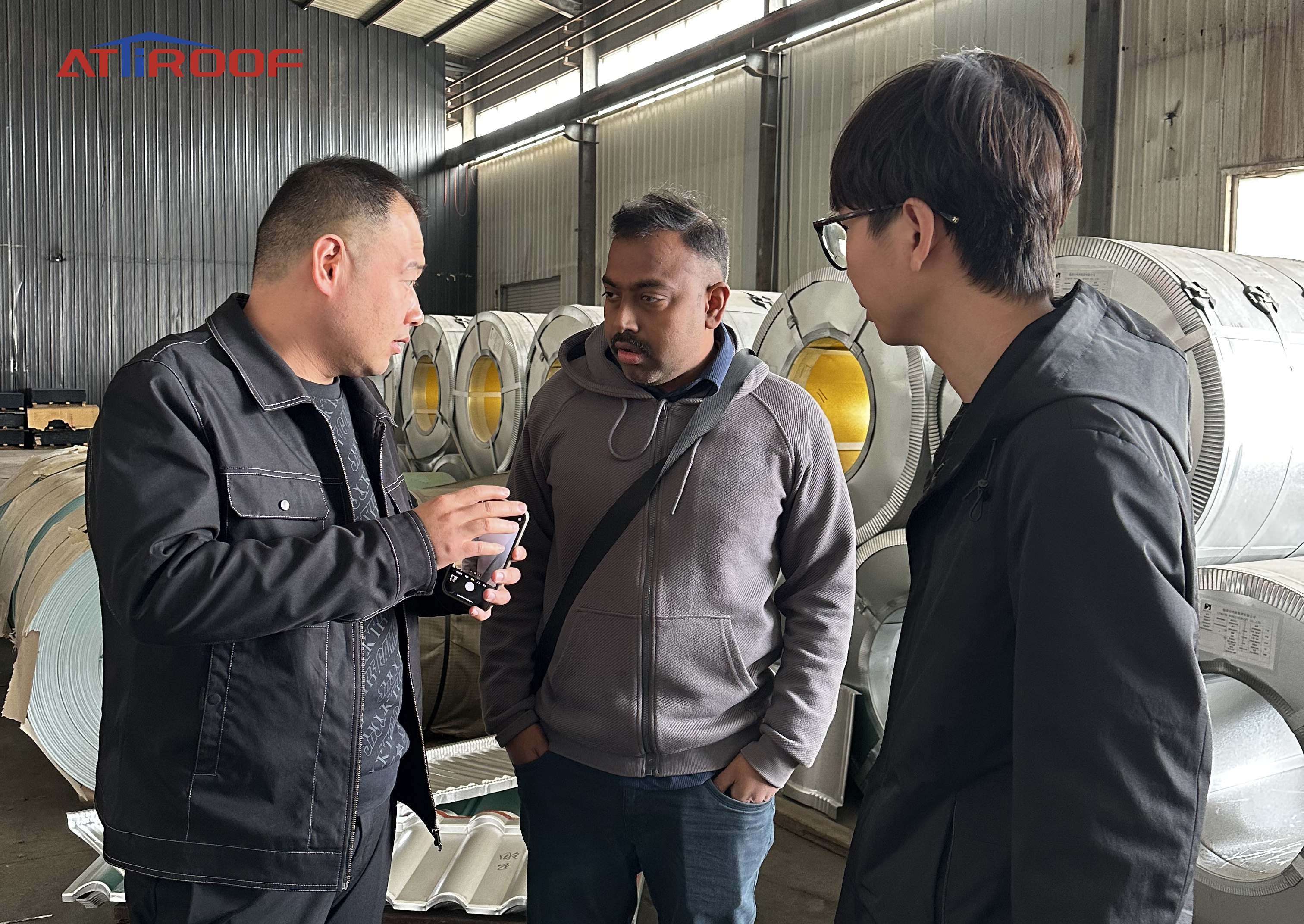 Discusión con proveedores sobre materiales de tejas metálicas recubiertas de piedra en una instalación de fabricación.